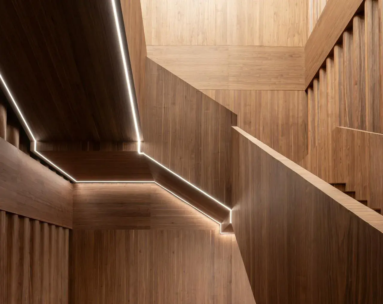 Detalle de iluminación lineal LED integrada en pasamanos y escaleras revestidas de madera fina.